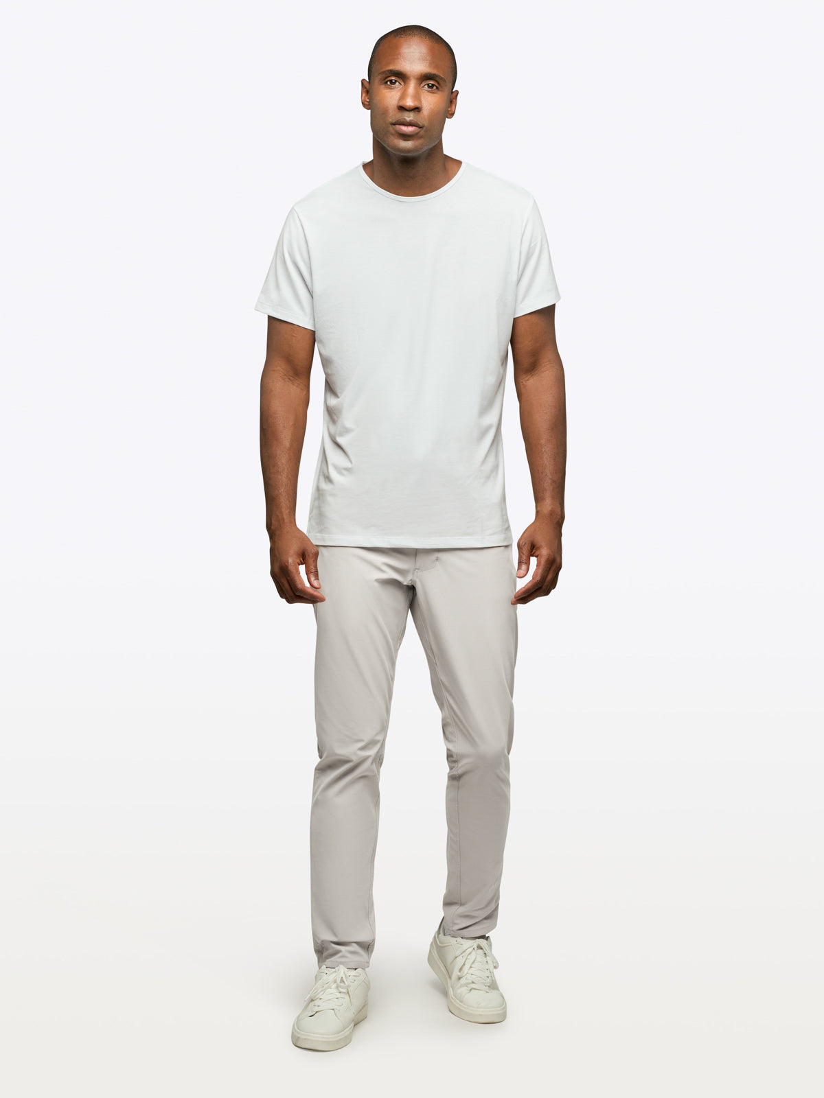 Man wearing a plain white t-shirt and light gray pants on a white background